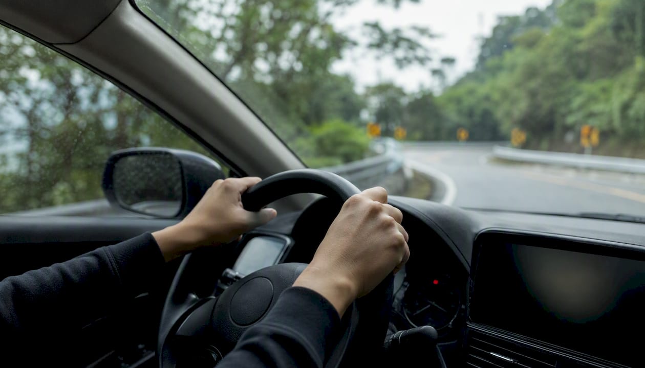 Hands on steering wheel driving mountain road
